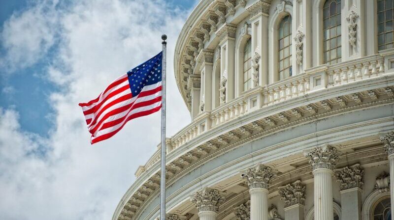 American flag flying in front of the US Capitol building dome, symbolising US pharmaceutical policy reform.